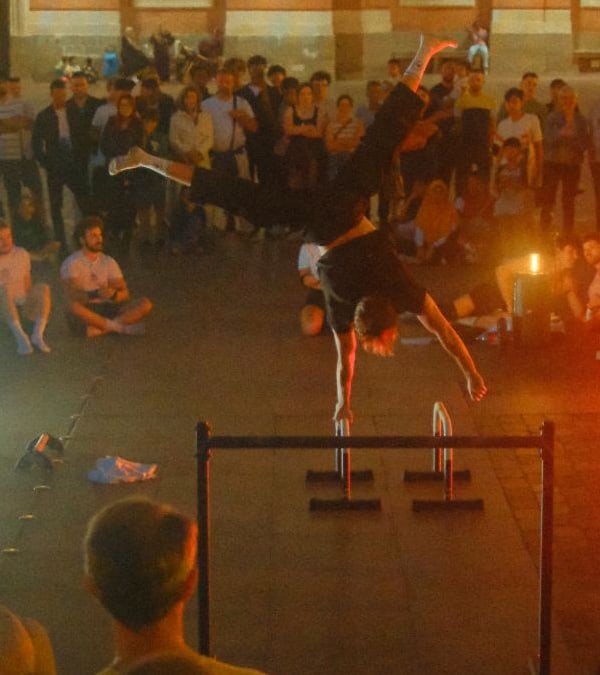 Mayeul en équilibre sur une main, sur des parallettes, devant le public de la place du Capitole à Toulouse